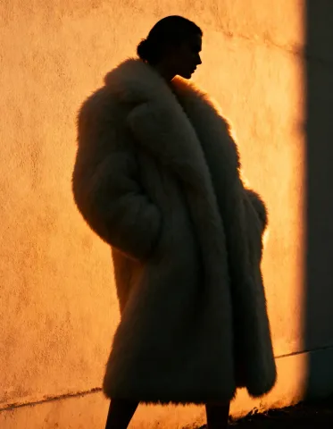 Golden wall silhouette — A fashion silhouette in a voluminous coat against a glowing orange wall, strong side light and minimal composition.