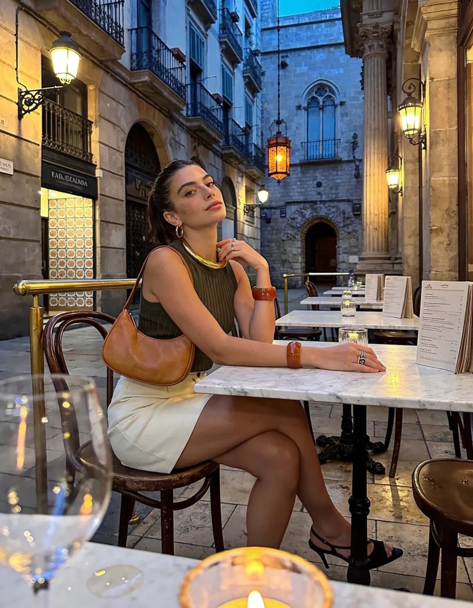 Evening terrace — A woman seated at an outdoor cafe in a narrow old street, blue evening architecture and warm lanterns.